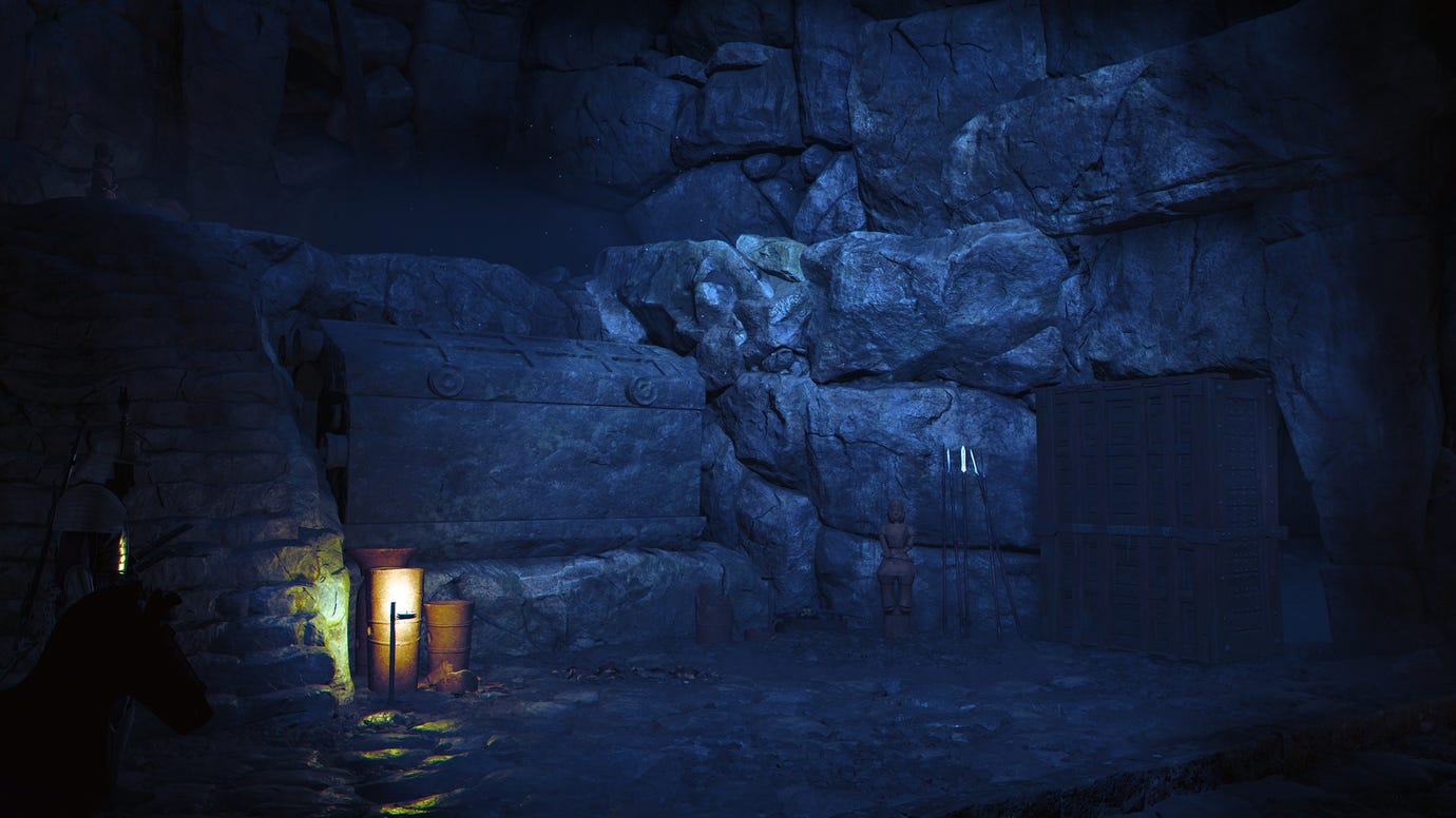 The interior of a kofun in Assassin's Creed Shadows. It is dark, with a small lantern light the only illumination. A large chest can be seen amongst the gloom.