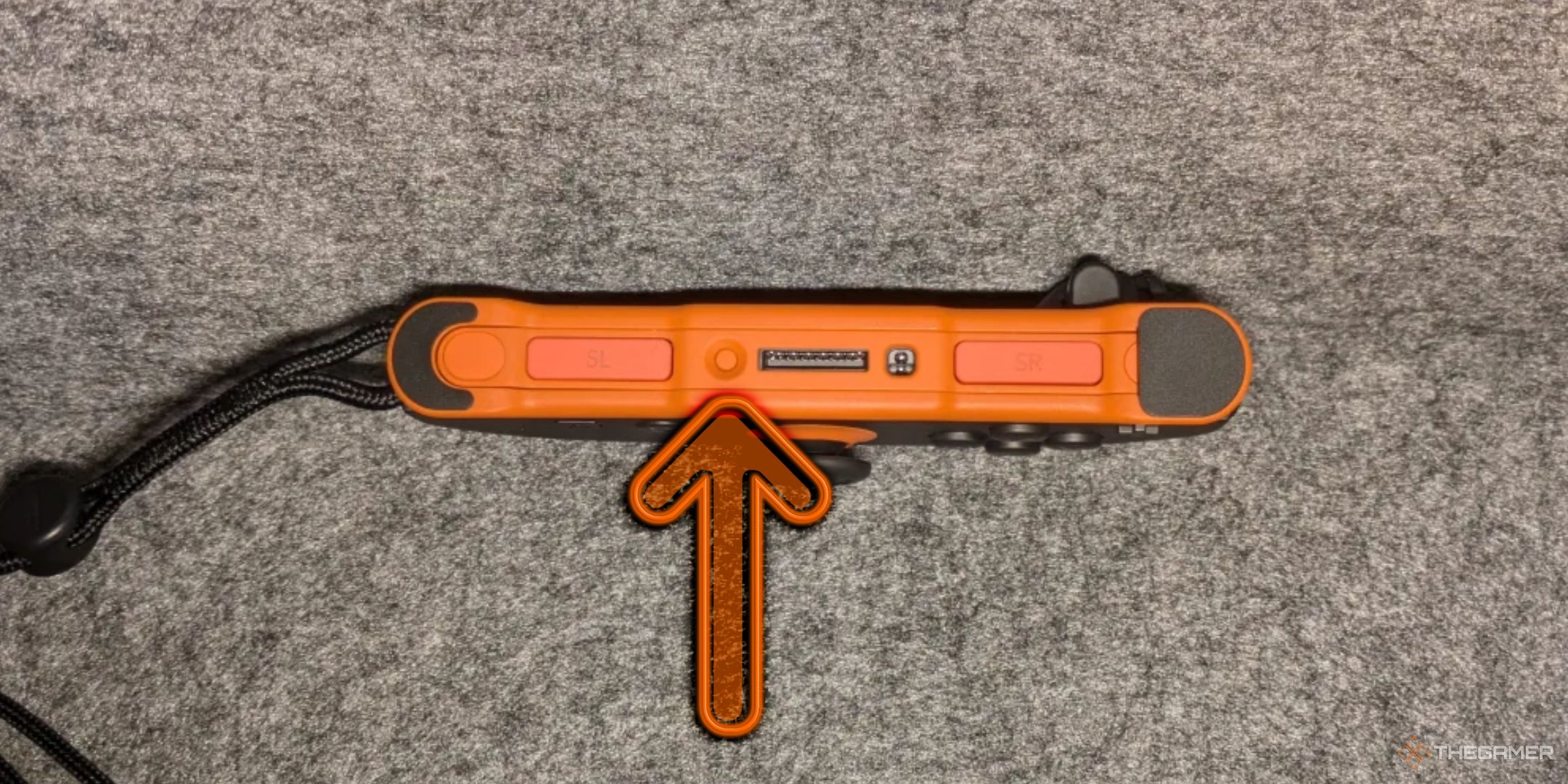 The side of an orange Nintendo Switch 2 Joycon, an arrow pointing at the sync button.