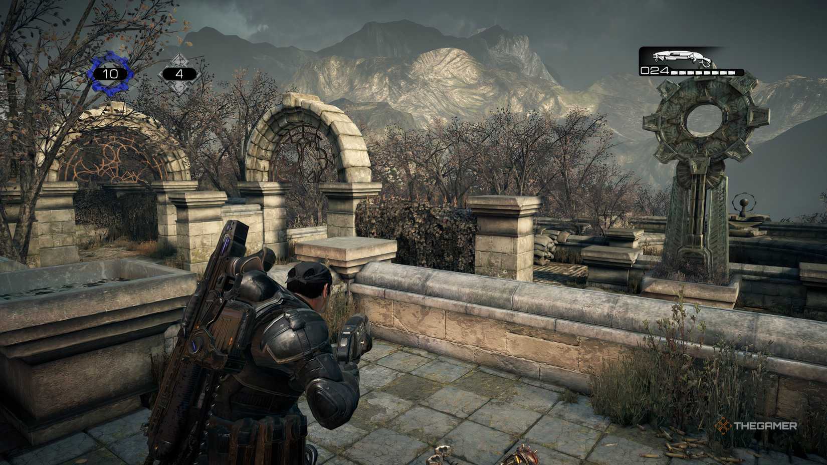 The player in a match looking mountains in the distance in Gears of War: Reloaded. There is a large COG statue infront of the player to the right. 